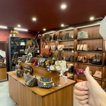 Four luxury handbags displayed on a shelf, including white, black, and patterned bags with metal details